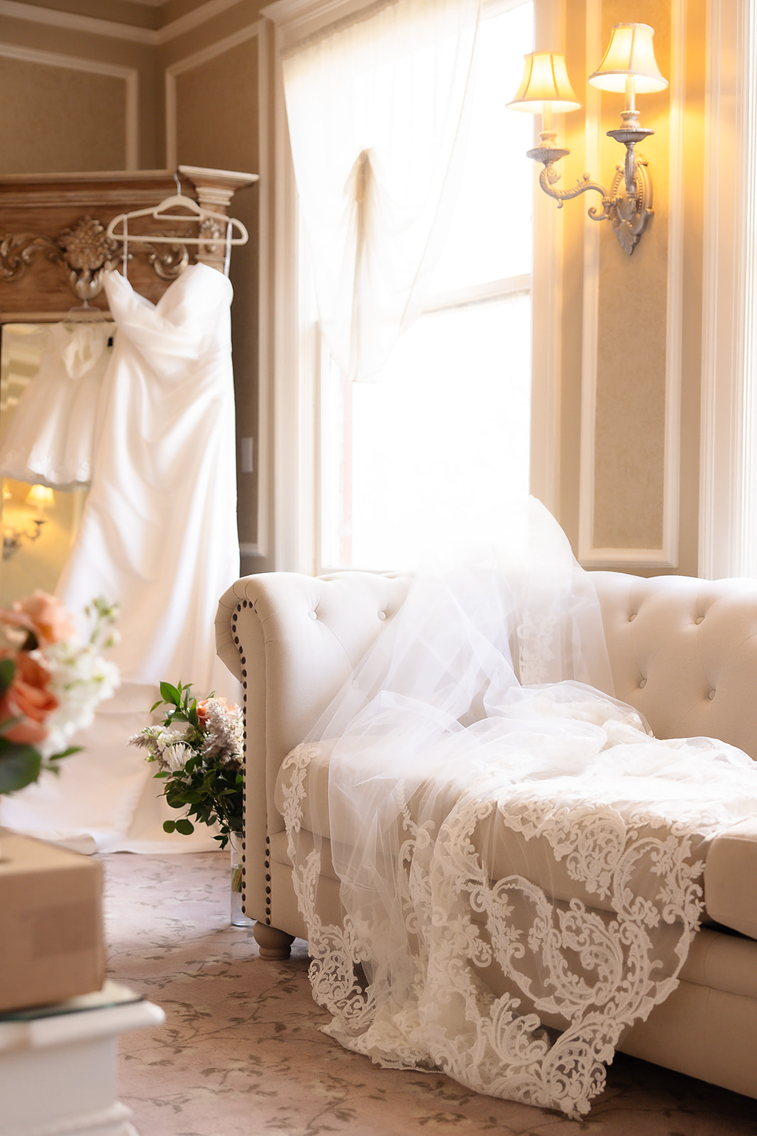 Bridal suite with wedding dress hanging and veil laying over couch