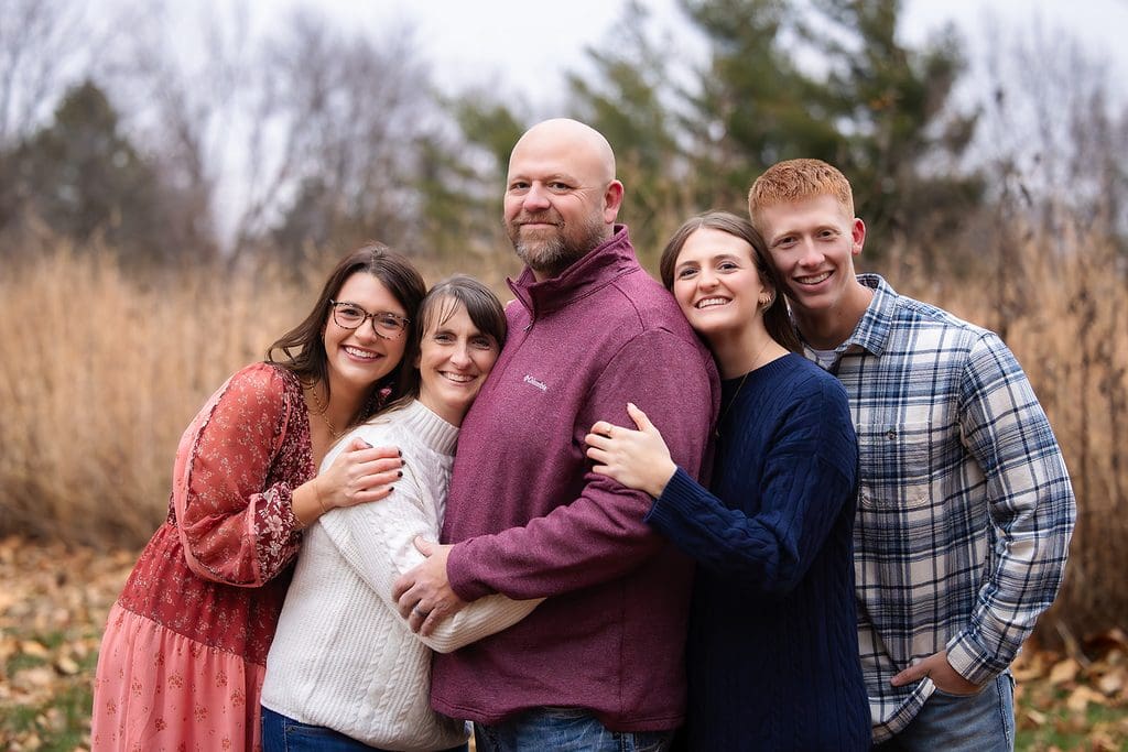 Family of five wearing beautiful coral, burgundy, and navy colors all hugging.
