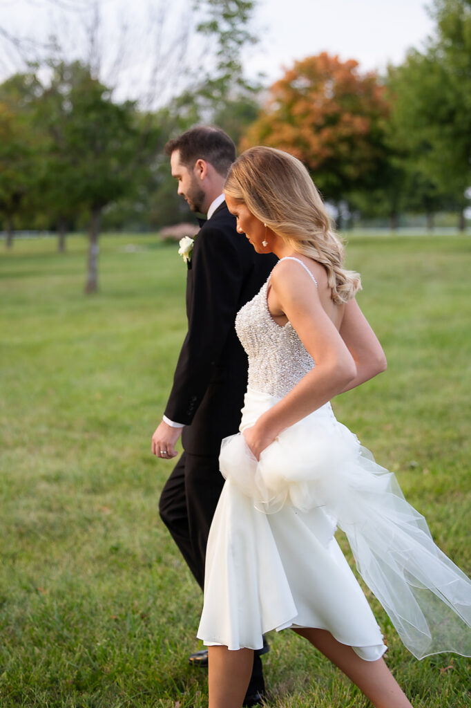 Bride holding her dress and walking with Groom at sunset