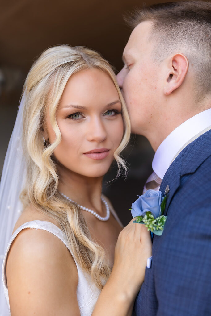 Bride looking at camera while groom kisses her hair