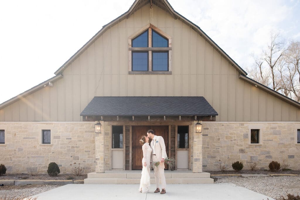 Bride and groom kissing, with groom holding pageant bouquet, outside of Cedar Lawn Farms in Topeka, Kansas.