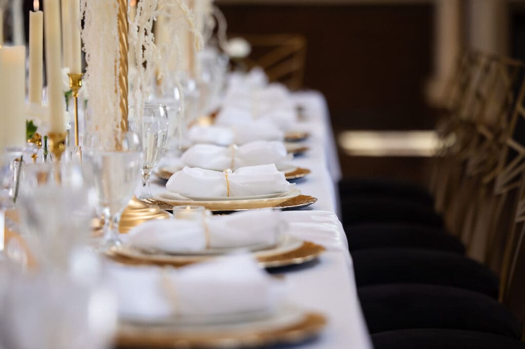 reception table with pearl ringed napkins, gold plates, gold and off-white candles, white and off-white florals inside the Great Overland Station in Topeka, Kansas